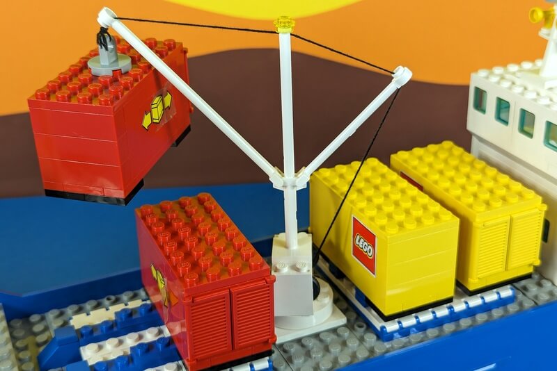 Die Szene zeigt das Verladen von Containern an einem Lego-Schiff.