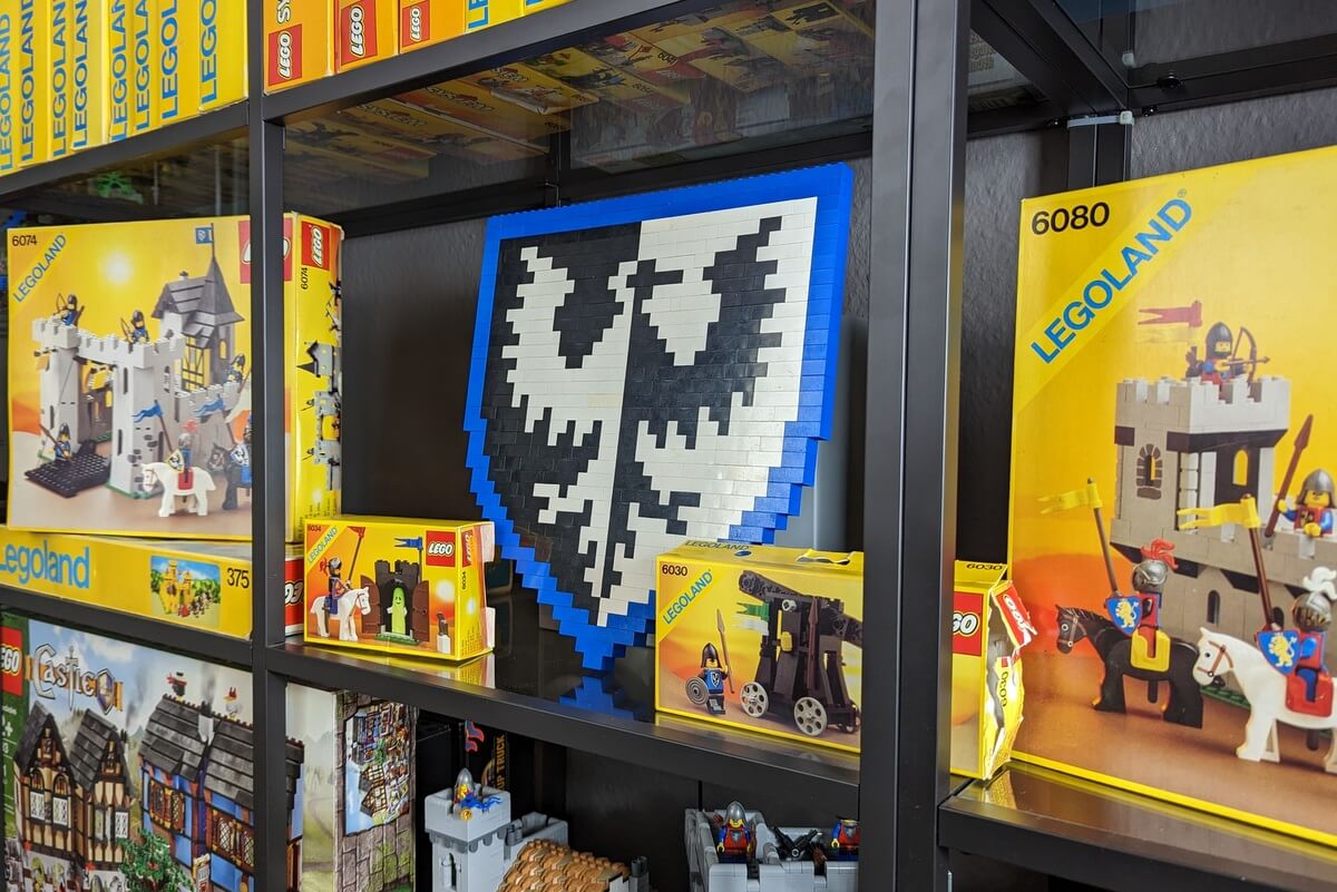Ein Regal voller alter Lego-Kartons mit dem gebauten Wappen der Falkenritter aus Lego-Steinen in der Mitte. 