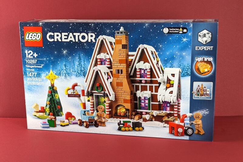 Die blaue Box vom originalverpackten Lebkuchenhaus von Lego aus dem Jahr 2019 vor weihnachtlichem Hintergrund in Rot.