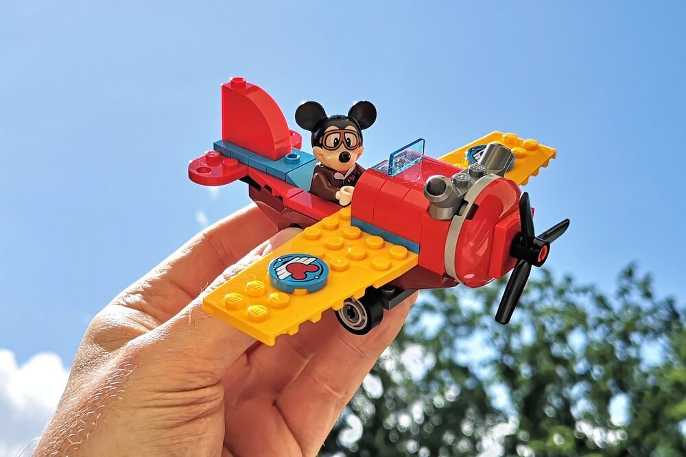 Der Doppeldecker aus LEGO mit MIcky-Maus-Figur in der Hand vor schönem blauem Himmel beim Spielen.
