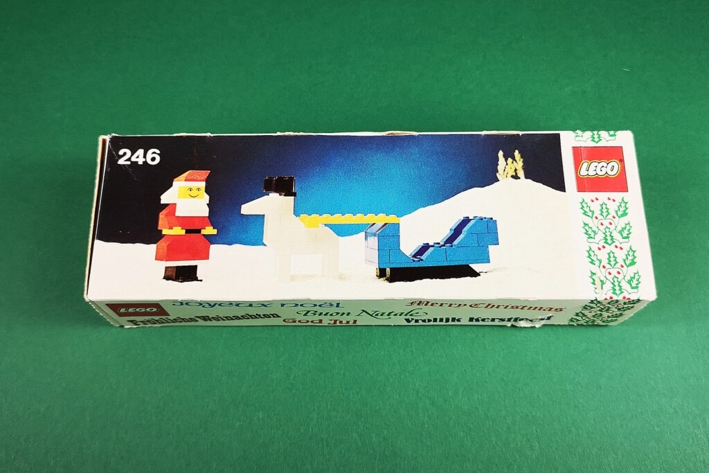 Zu sehen ist die sehr seltene Original-Verpackung vom LEGO-Weihnachtsset 246. Darauf ist ein aus LEGO-Steinen gebauter Weihnachtsmann mit seinem Schlitten und einem Rentier zu sehen. Das Artwork sieht typisch 70er-Jahre aus.
