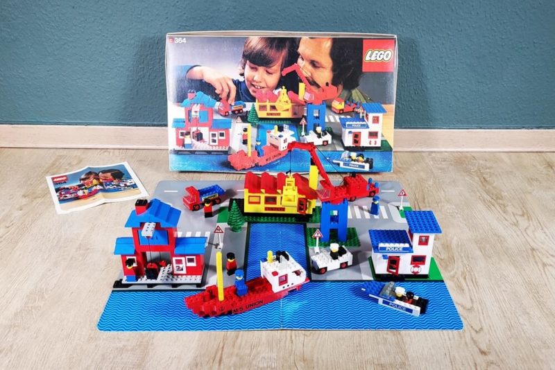 Das komplette LEGO-Set 364 auf einem Bild. Mit Originalkarton, Bauanleitung, Baseplate, Häuseren , Fahrzeugen und Minifiguren.