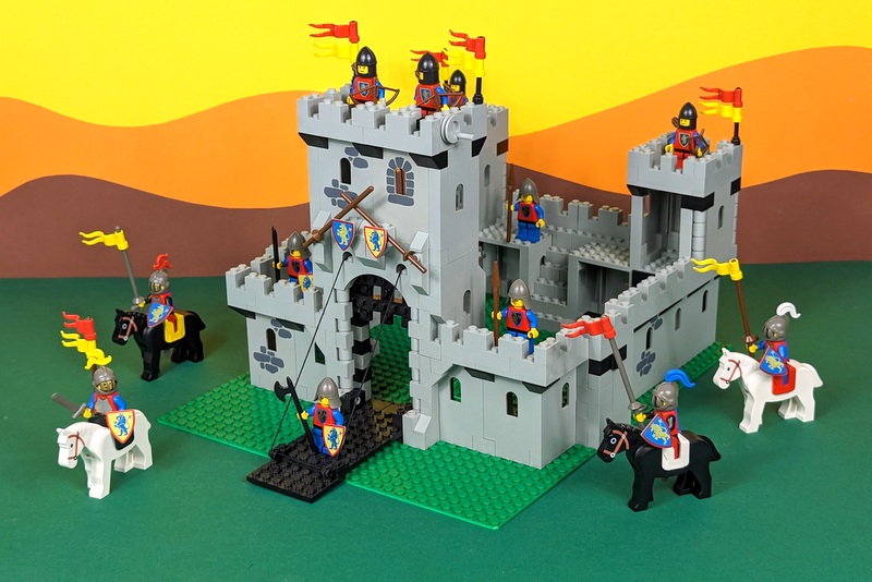 Die Lego-Burg mit der Setnummer 6080 aufgebaut mit allen Figuren und Pferden vor einem klassischen bunten Papp-Hintergrund wie in den alten Katalogen.