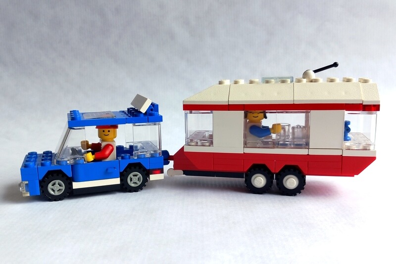 Blaues Lego-Auto mit weiß-rotem-Wohnwagen von der Seite.