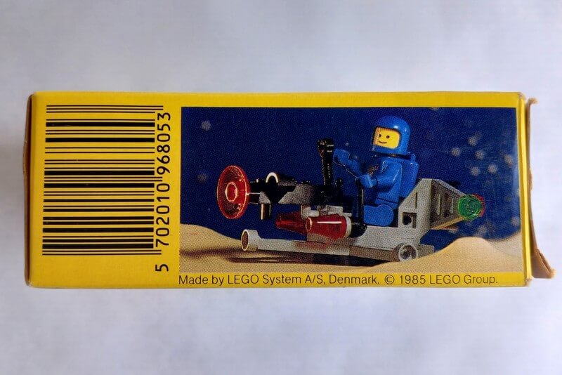 Die Unterseite ist links in gelb gehalten mit einem Barcode und rechts ist ein weiteres Bild von dem Legomodell mit blauem Astronauten zu sehen.