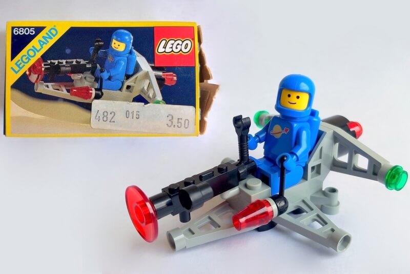 Im Hintergrund liegt die Original-Verpackung von Set 6805 von 1985 und im Vordergrund steht das fertig gebaute Lego-Set mit der Raumfahrer-Figur.