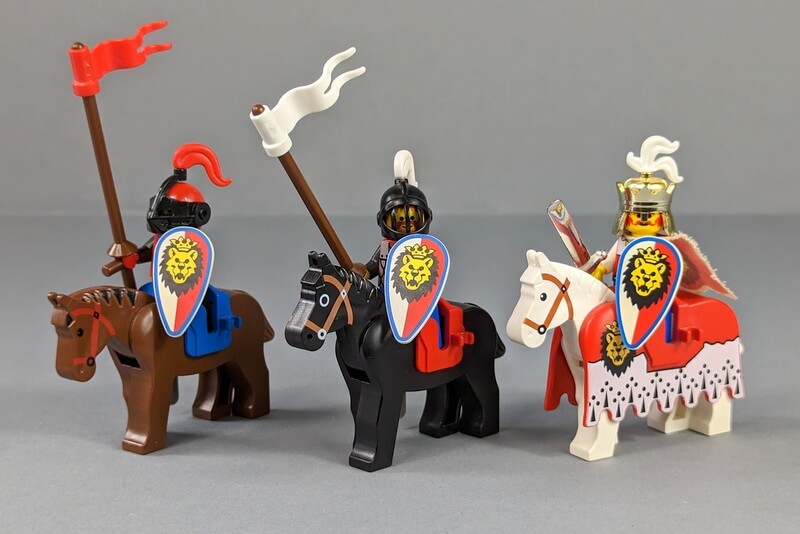 Drei Lego-Ritter mit Pferden. Darunter der König mit Helmkrone, Umhang und Pferd mit Pferdedecke.