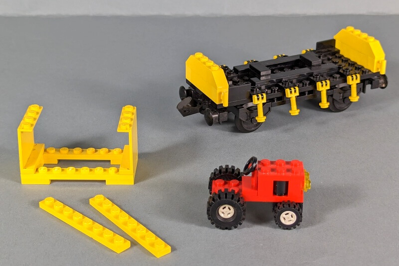Entladener Frachtwaggon aus Lego-Steinen mit kleinem Traktor davor.