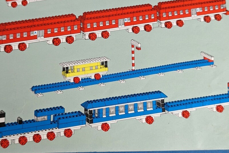 Das Detailbild zeigt einen gelben Eisenbahnwagen, der auf Schienen aus alten Lego-Steinen rollt.