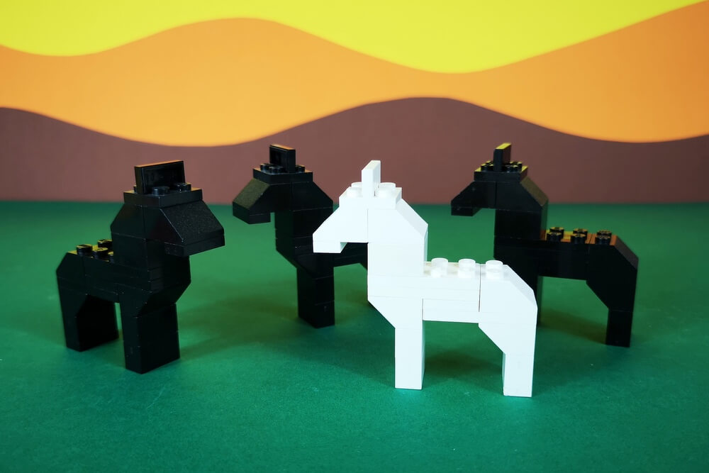 Die Pferde der 70er-Jahre sind komplett aus Bausteinen gebaut. Auf dem Bild sind drei schwarze Baustein-Pferde und ein weißes Pferd zu sehen.