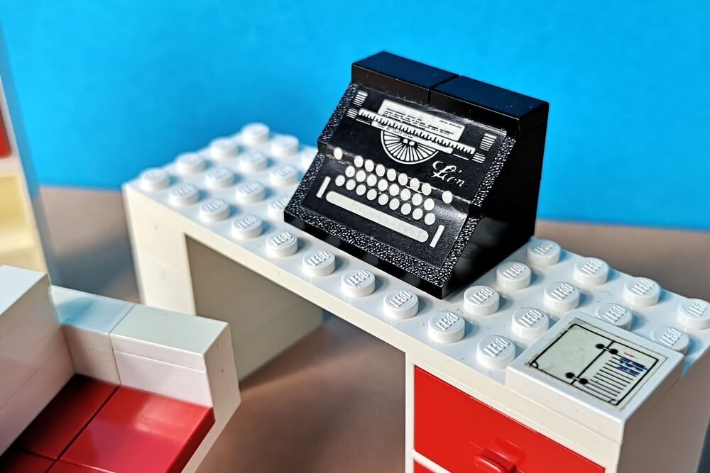 Eine Schreibmaschine aus schwarzen Lego-Steinen mit einem Sticker, der die Tastatur nachahmt. Sehr dekorativer klassischer Look der 70er-Jahre.