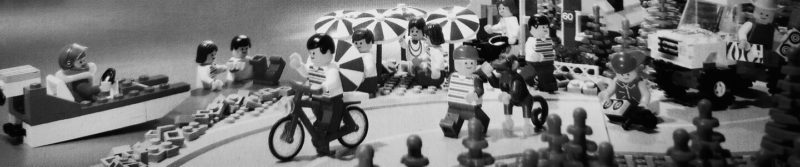 Zu sehen sind viele LEGO-Männchen in einer Stadtszene. Ein kleines LEGO-Boot, eine LEGO-Fahrrad, Sonnenschirme und ein LEGO-Safari-Jeep sind zu sehen.