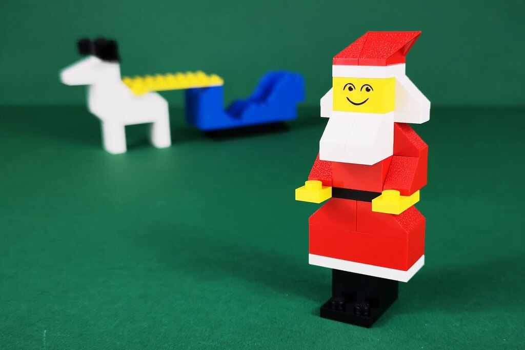 Ein Weihnachtsmann aus LEGO-Steinen aus dem Jahr 1977. Im Hintergrund ist ganz klein sein Schlitten und sein Rentier zu sehen.