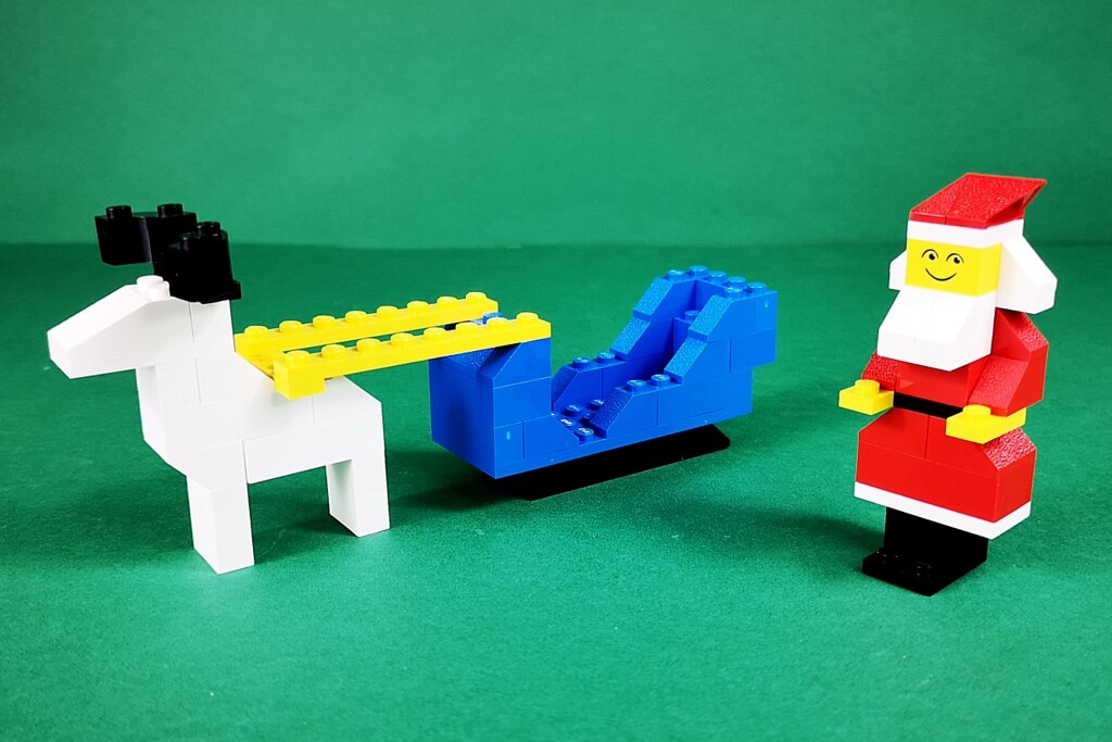 LEGO-Weihnachtsmann mit Rentierschlitten im Stil der 70er-Jahre. Das Modell ist sehr noppig und eckig in den Farben weiß, blau, gelb, rot und schwarz.