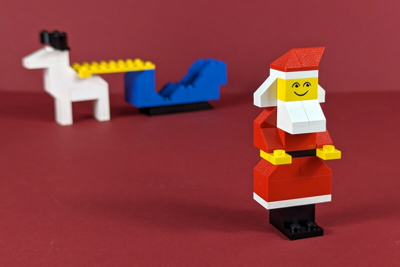 Ein Weihnachtsmann aus LEGO-Steinen aus dem Jahr 1977. Im Hintergrund ist ganz klein sein Schlitten und sein Rentier zu sehen.