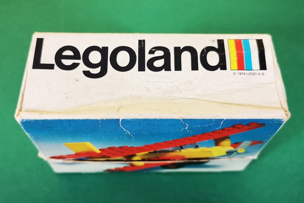 Der Legoland-Schriftzug der späten 70er-Jahre in schwarzer Schrift auf weißem Grund mit der fünffarbigen LEGO-Fahne daneben.