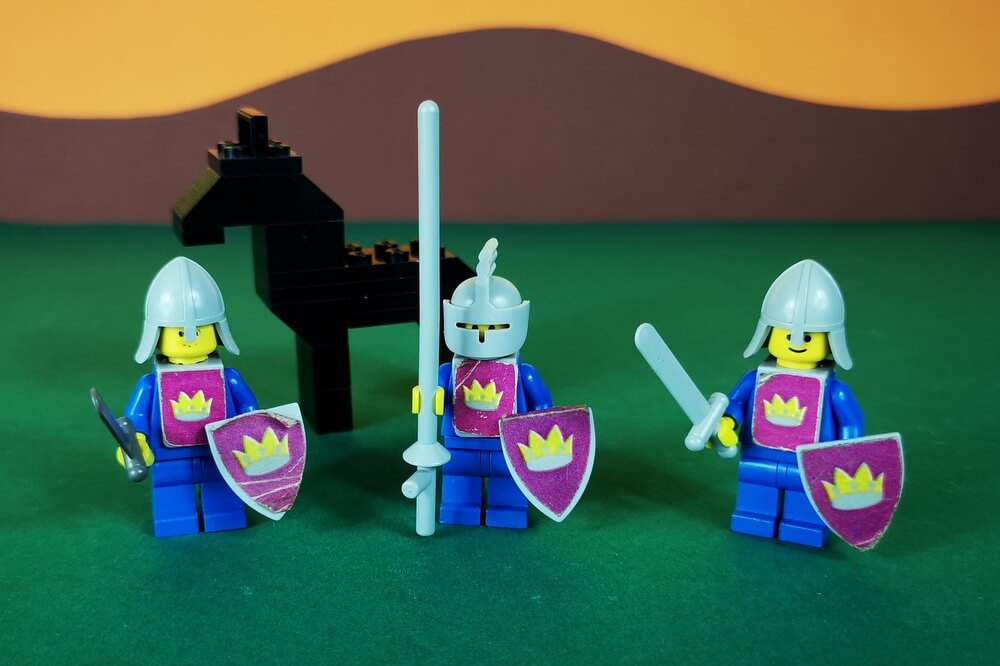 In der Mitte ist ein Ritter mit Helm, Visier, Lanze. Schild und Pferd. Rechts und links von ihm sind zwei Begleit-Soldaten mit Schwertern und Schilden. Alle Schild tragen das Wappen der gelben Burg.