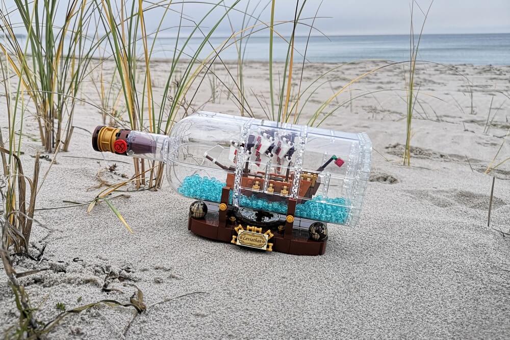 Ein Flaschenschiff aus LEGO-Steinen am Strand der Ostsee im Dezember. Im Hintergrund ist die blaue Ostsee zu sehen. Vorn ist schöner Sand und Strandgras. Mittendrin steh das LEGO-Modell.