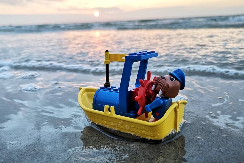 LEGO-Boot in Gelb mit Willy Walross aus der Fabuland-Serie am Steuer des Bootes. In der Brandung der Ostsee mit Sonnenuntergang im Hintergrund.